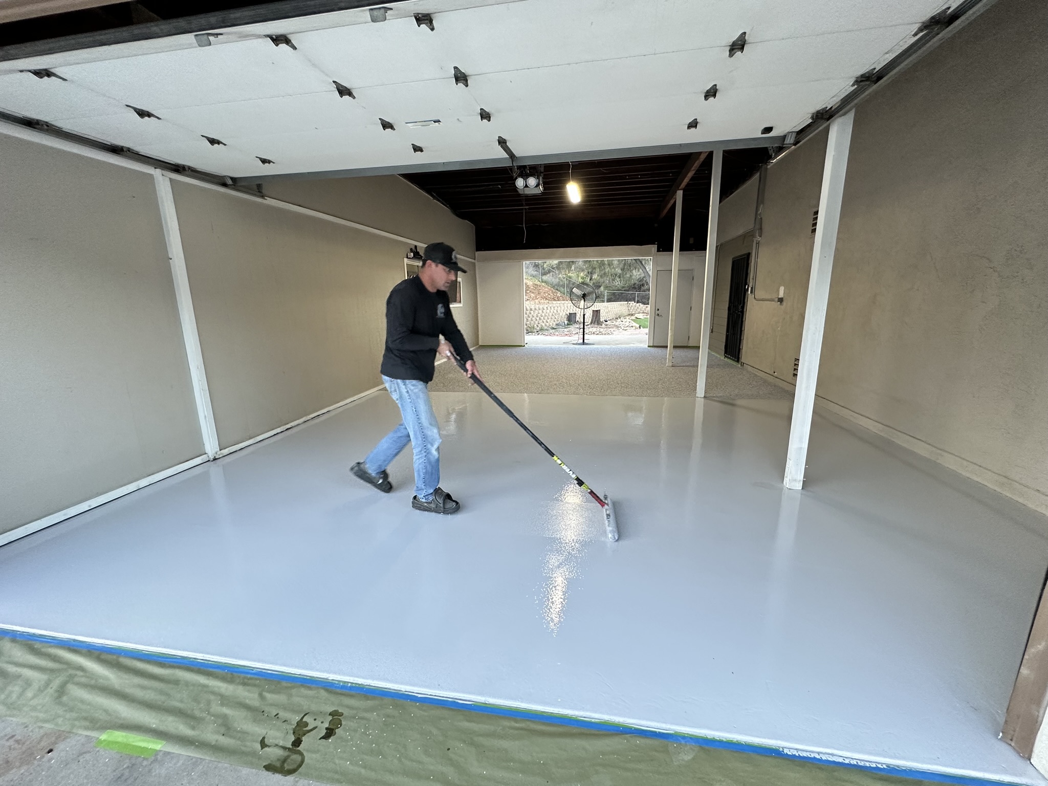 Man applying a fresh epoxy coating to a garage floor, demonstrating the process of enhancing durability and aesthetics in a residential space.