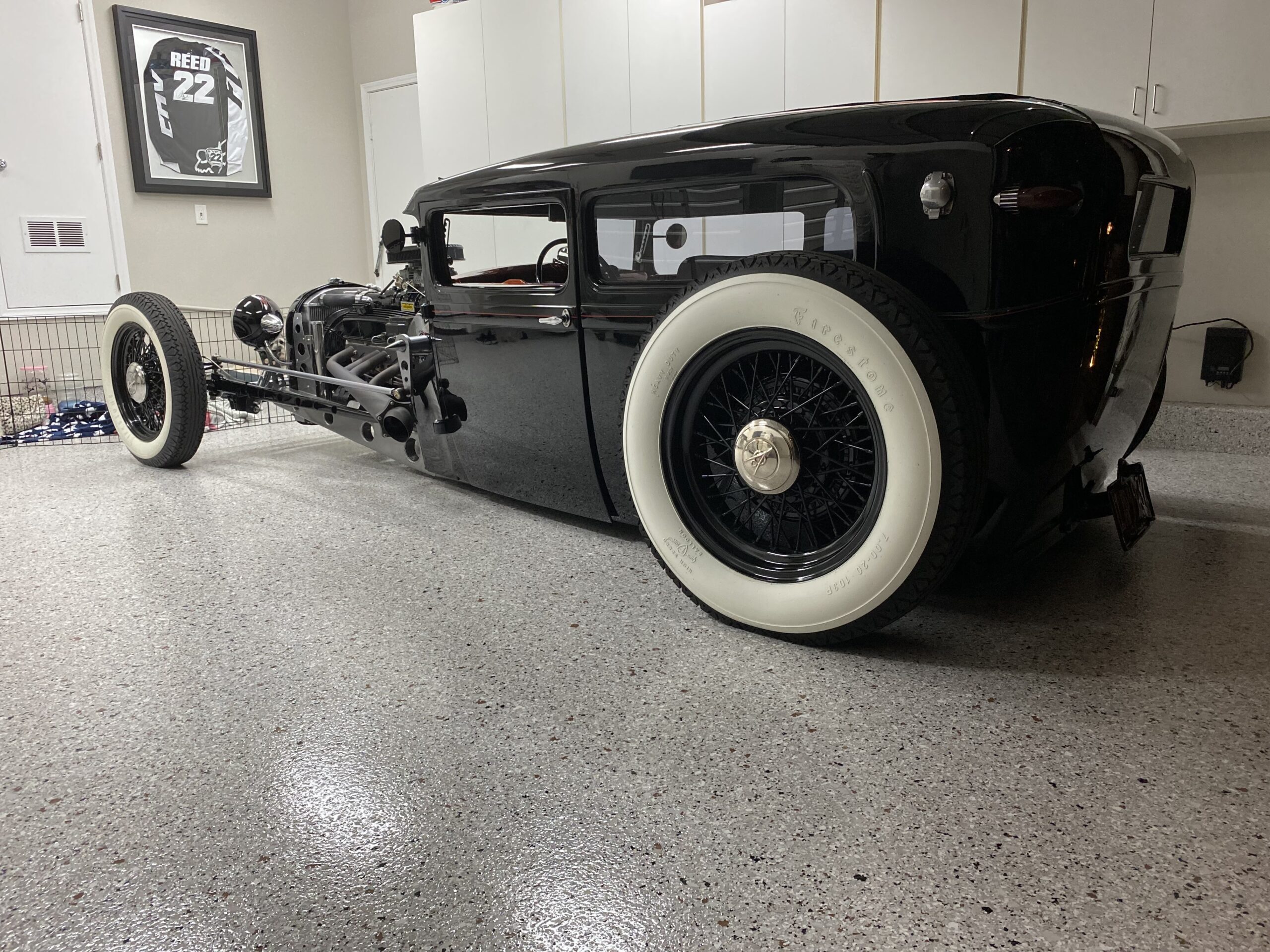 Classic black hot rod with whitewall tires parked on a glossy epoxy garage floor, showcasing durability and aesthetic appeal in a well-organized garage space.