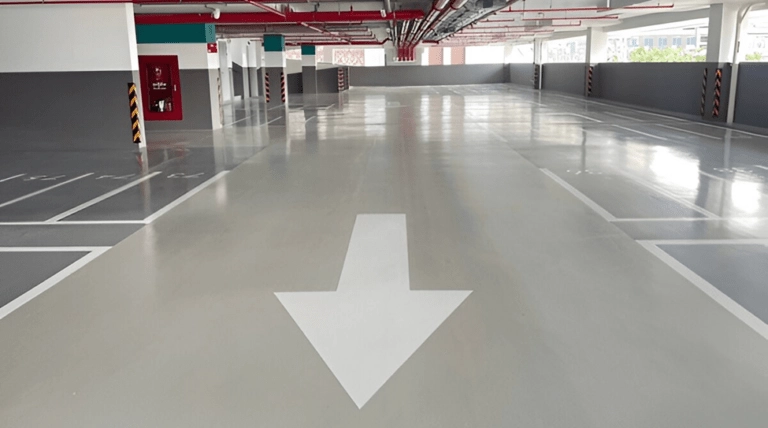 Epoxy-coated parking garage floor with directional arrow and marked parking spaces, illustrating durable flooring solutions for commercial spaces.