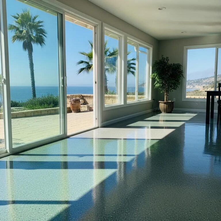 Epoxy flooring in a coastal home, showcasing durability and moisture resistance, with large windows revealing an ocean view and palm trees.