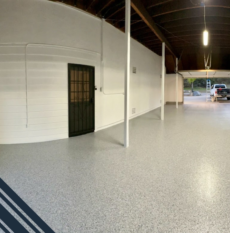 Clean, polished epoxy flooring in a garage setting with a black door and white walls, showcasing a recent transformation by Pristine Epoxy Floor Coatings in San Diego.