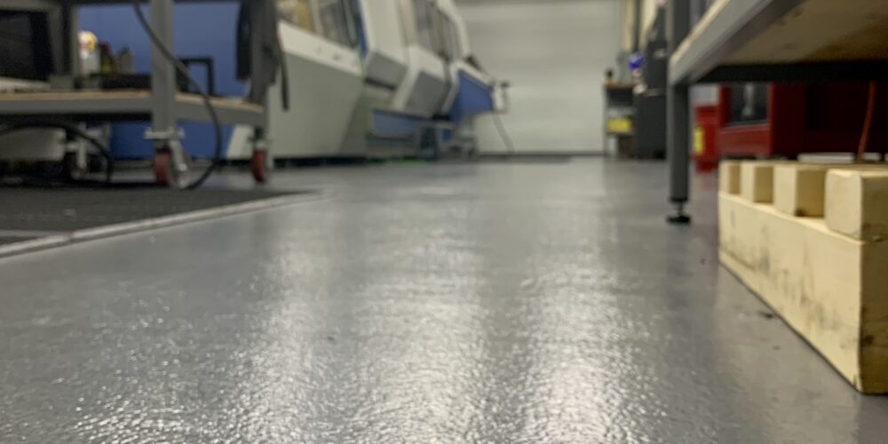 Epoxy flooring in a commercial workshop, showcasing a slip-resistant surface designed for safety and easy maintenance, with visible machinery and workstations in the background.