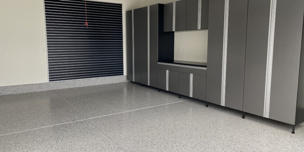 Epoxy-coated garage floor with a smooth, glossy finish, complemented by modern cabinetry and a slat wall for organization, showcasing durability and aesthetic appeal in a commercial space.