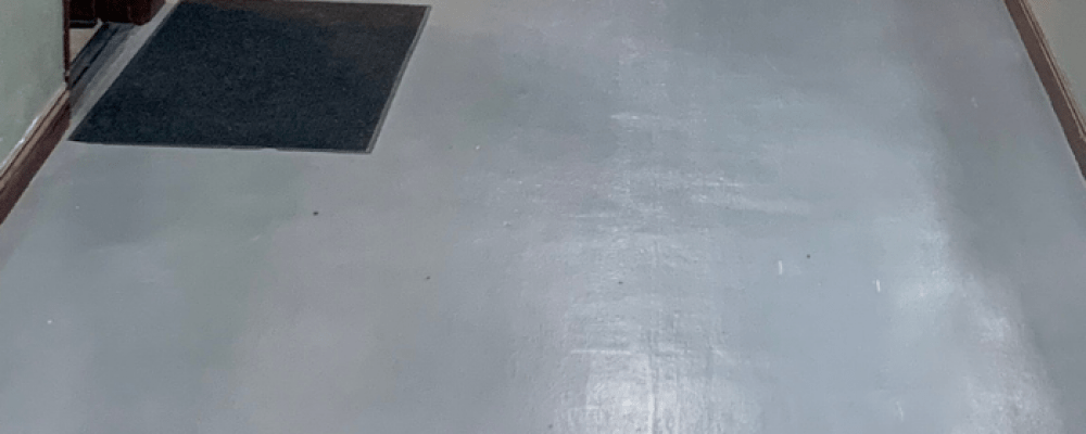 Epoxy flooring in a commercial space, featuring a smooth, non-porous surface with a black mat at the entrance, illustrating durability and ease of maintenance.