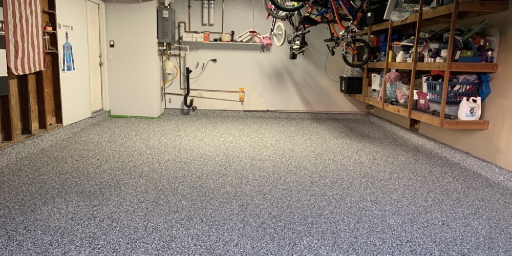 Epoxy-coated garage floor with decorative flake finish, showing organized storage shelves and bicycles, emphasizing durability and aesthetic appeal for residential spaces.