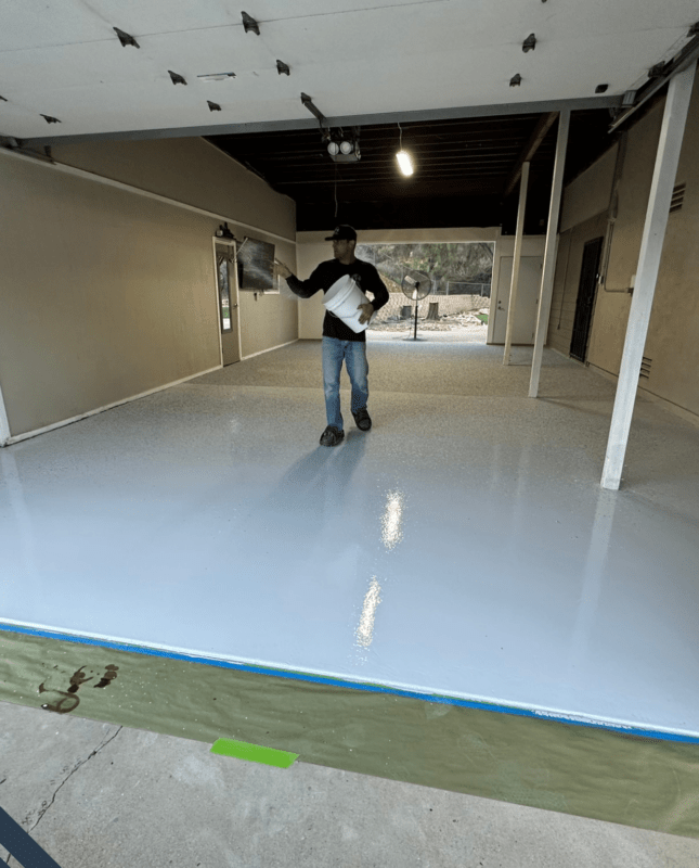 Man applying epoxy flooring in a residential garage, showcasing the smooth, glossy surface and professional installation techniques.