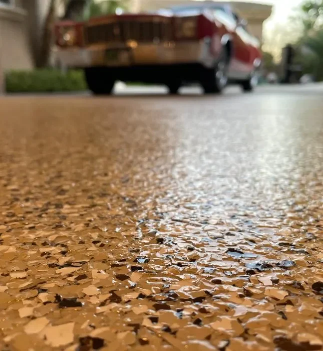 Glossy polyaspartic garage floor coating with decorative flakes and a classic red car in the background, showcasing durability and aesthetic appeal for garage refinishing projects.